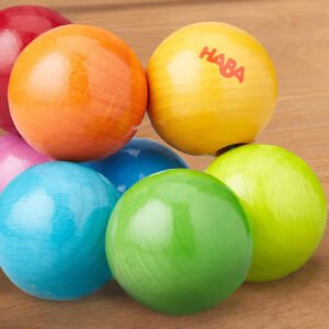 Close up of Magica Wooden Clutching Toy made of of wooden balls in various shades of pink, orange, yellow, blue, green, and red on a light wooden surface.