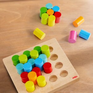 A wooden board with an array of brightly colored cylindrical pegs, additional pegs in orange, yellow, pink, and blue are scattered around the board on a light wooden surface.