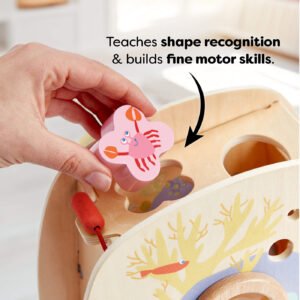 A hand placing a pink crab-shaped block into a matching slot on a wooden toy. Text reads 