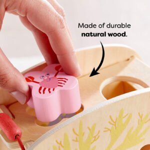 Child inserting a pink crab-shaped wooden block into a matching slot on a wooden toy. Text reads 